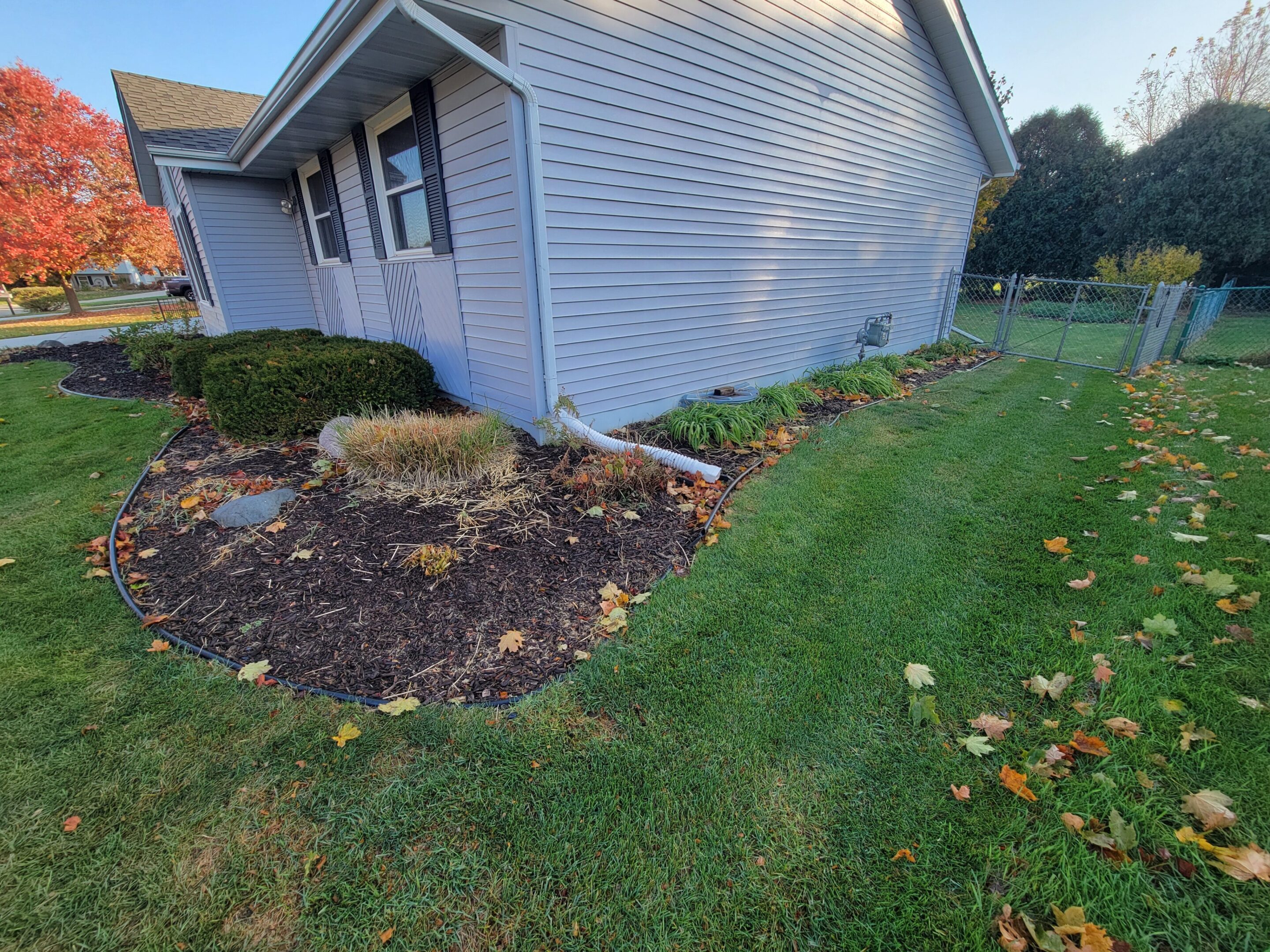 Corner of a house with a garden bed and green lawn.