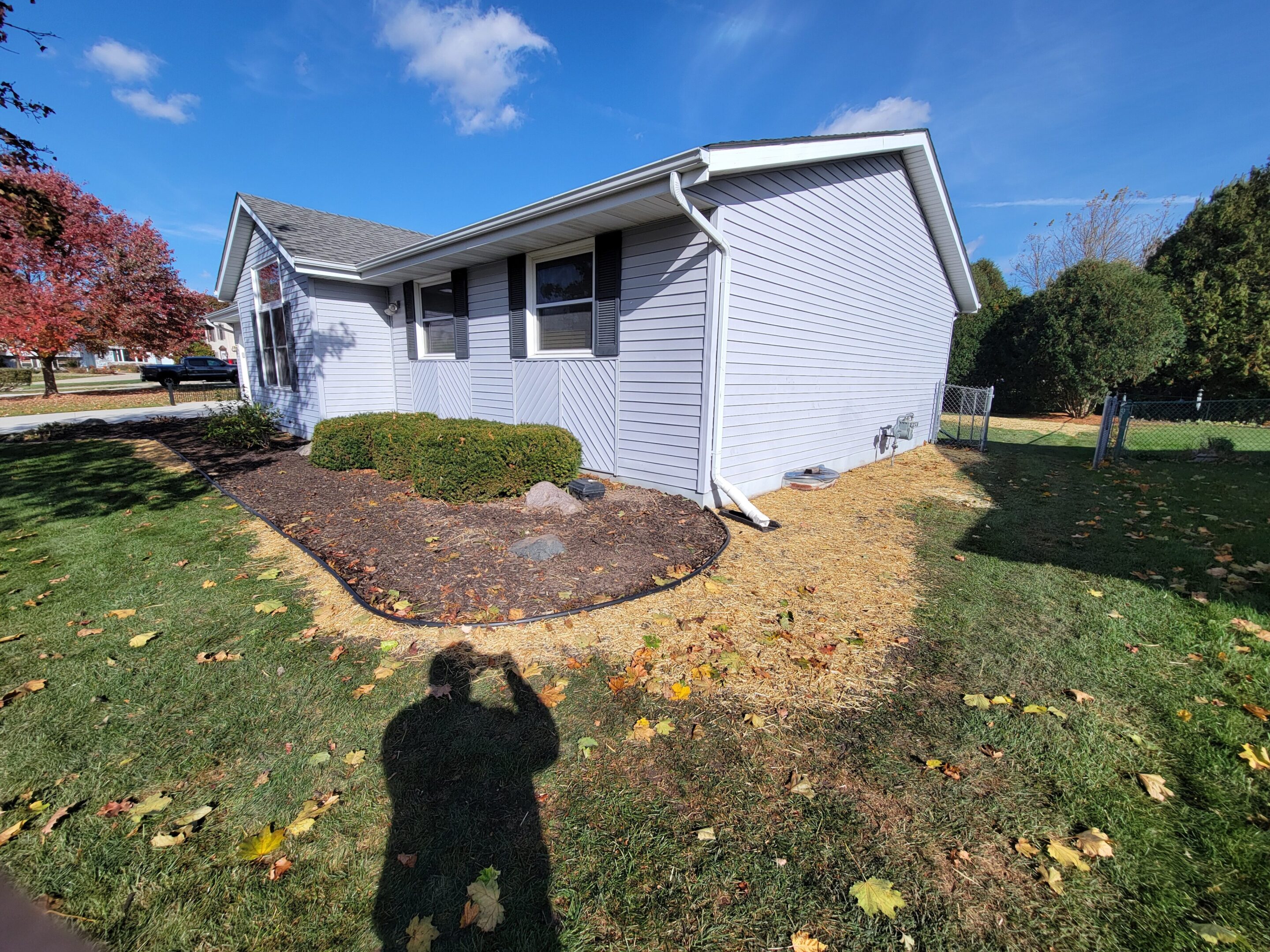 A white house with a garden bed and a shadow of a person taking the photo.