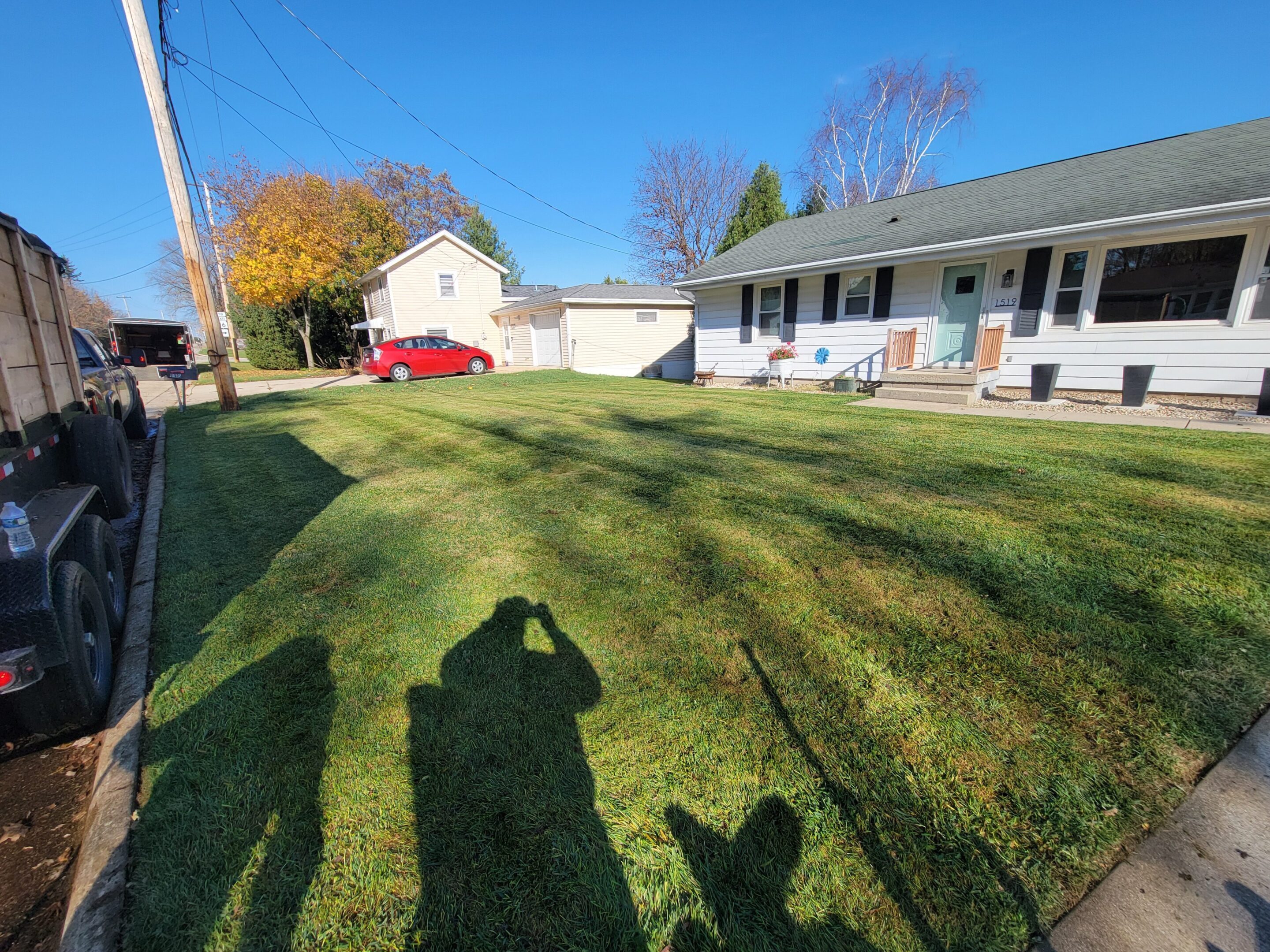 A sunny backyard with a neatly mowed lawn and a shadow of a person taking a photo.