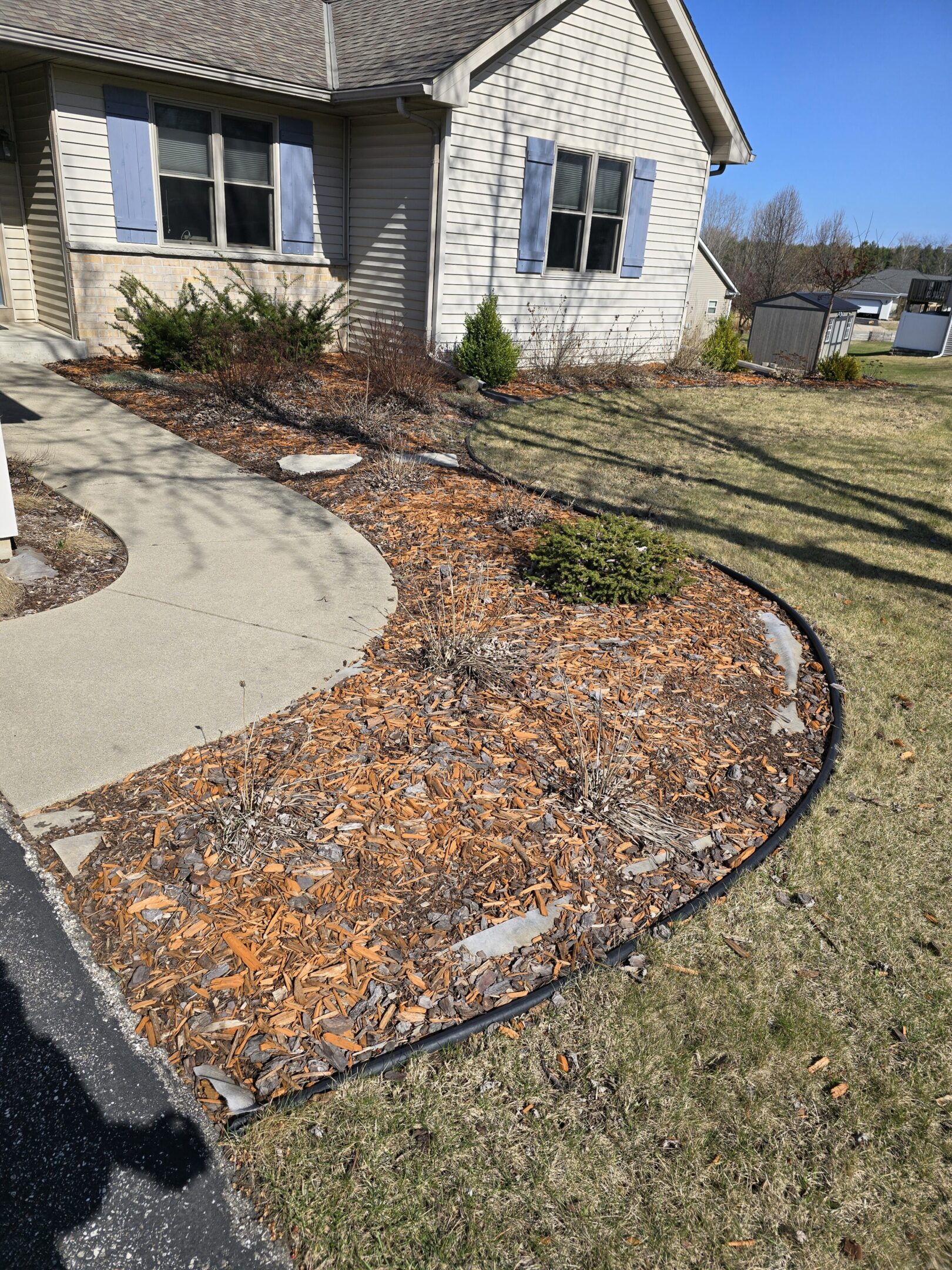 Mulched garden bed with small plants beside a house.