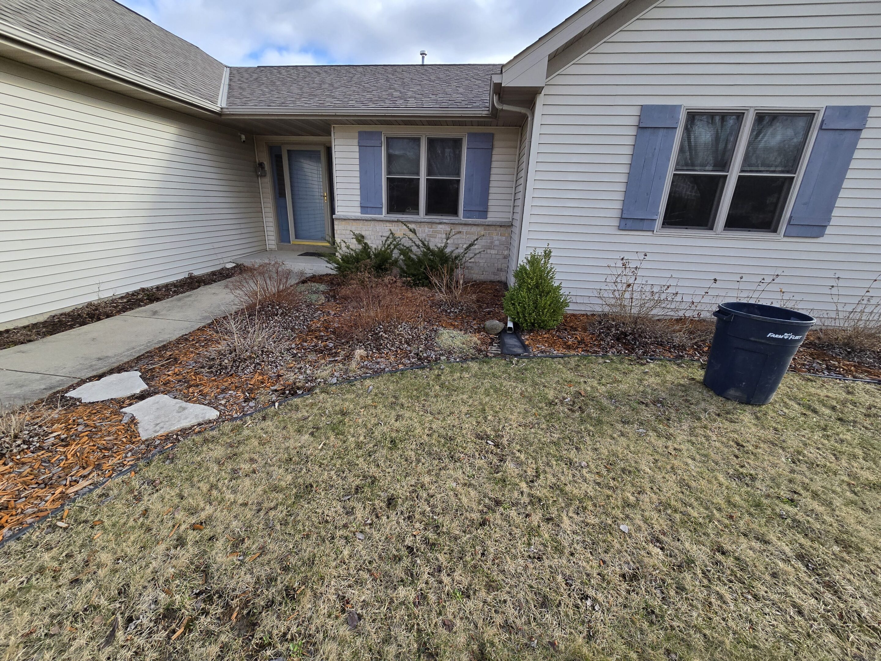 A front yard with a small garden bed and lawn area in front of a white brick house.