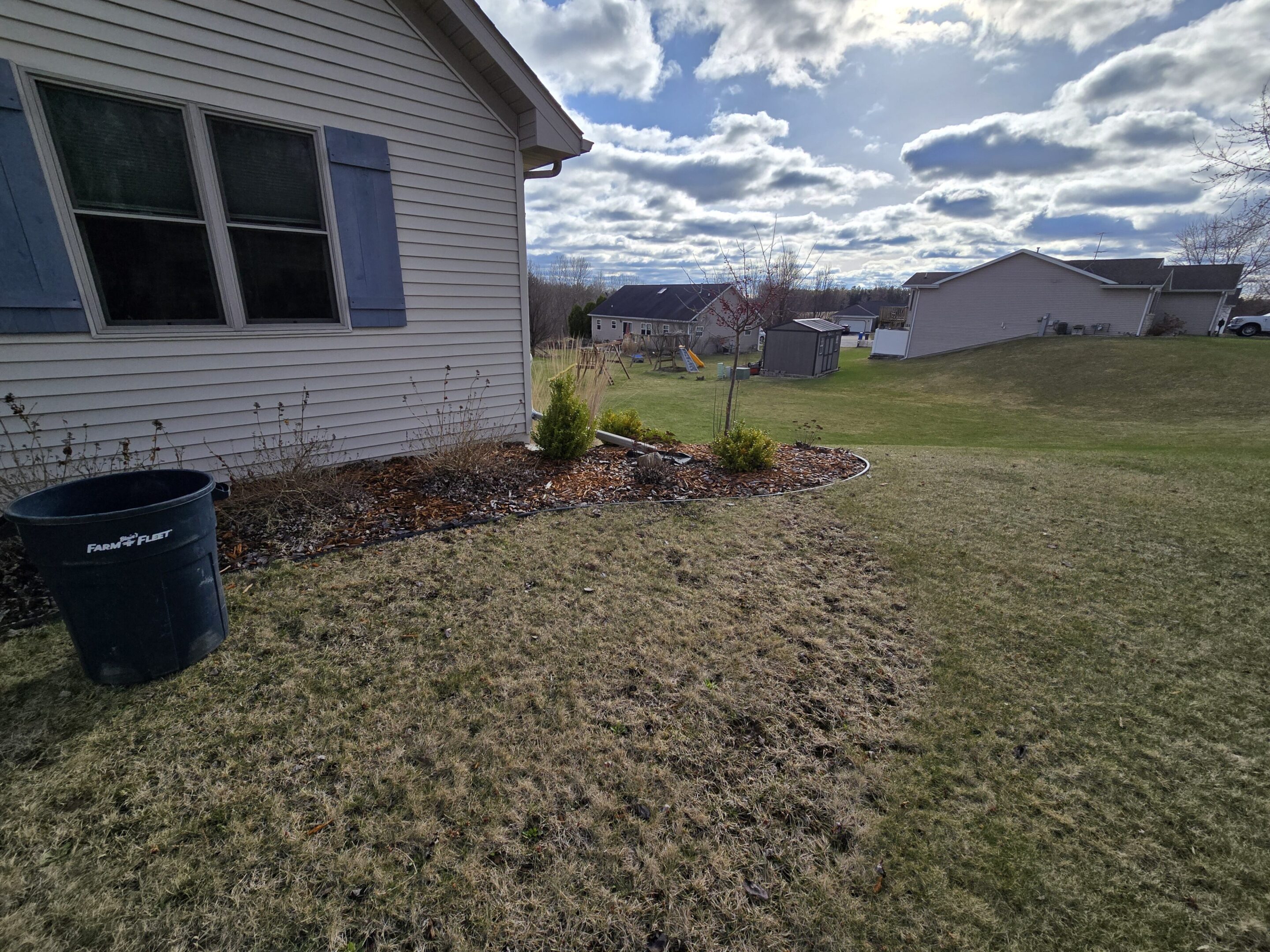 Backyard garden beside a house with cloudy sky.