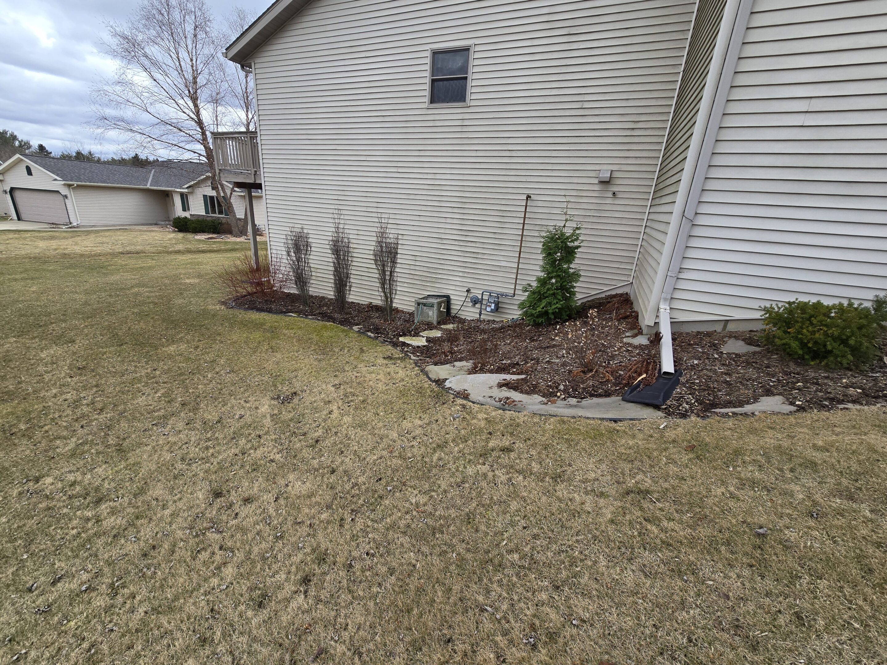Neatly mulched garden bed with young plants along a house's exterior wall.