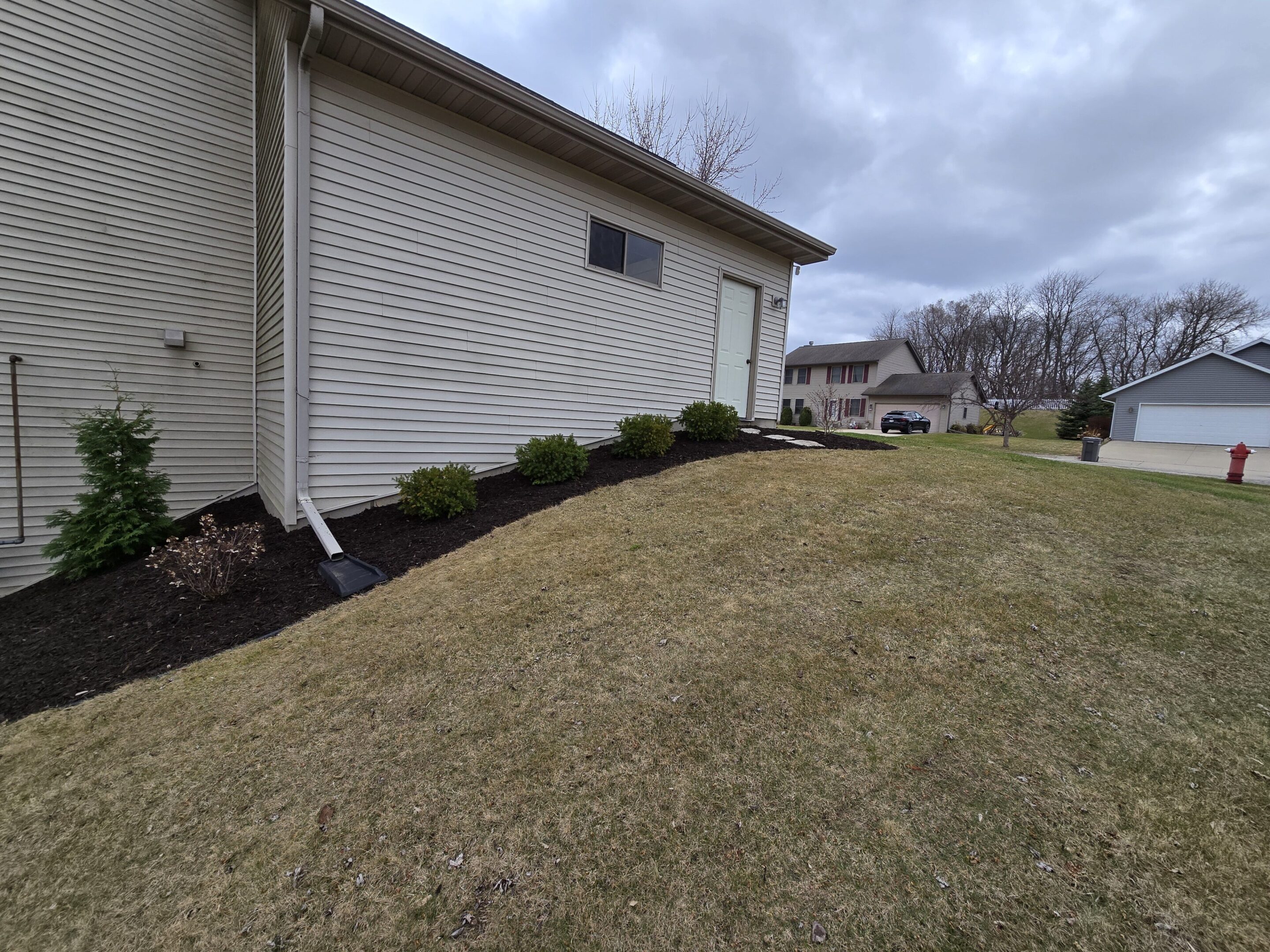 A house with newly planted shrubs along its foundation and a neatly mulched garden bed.