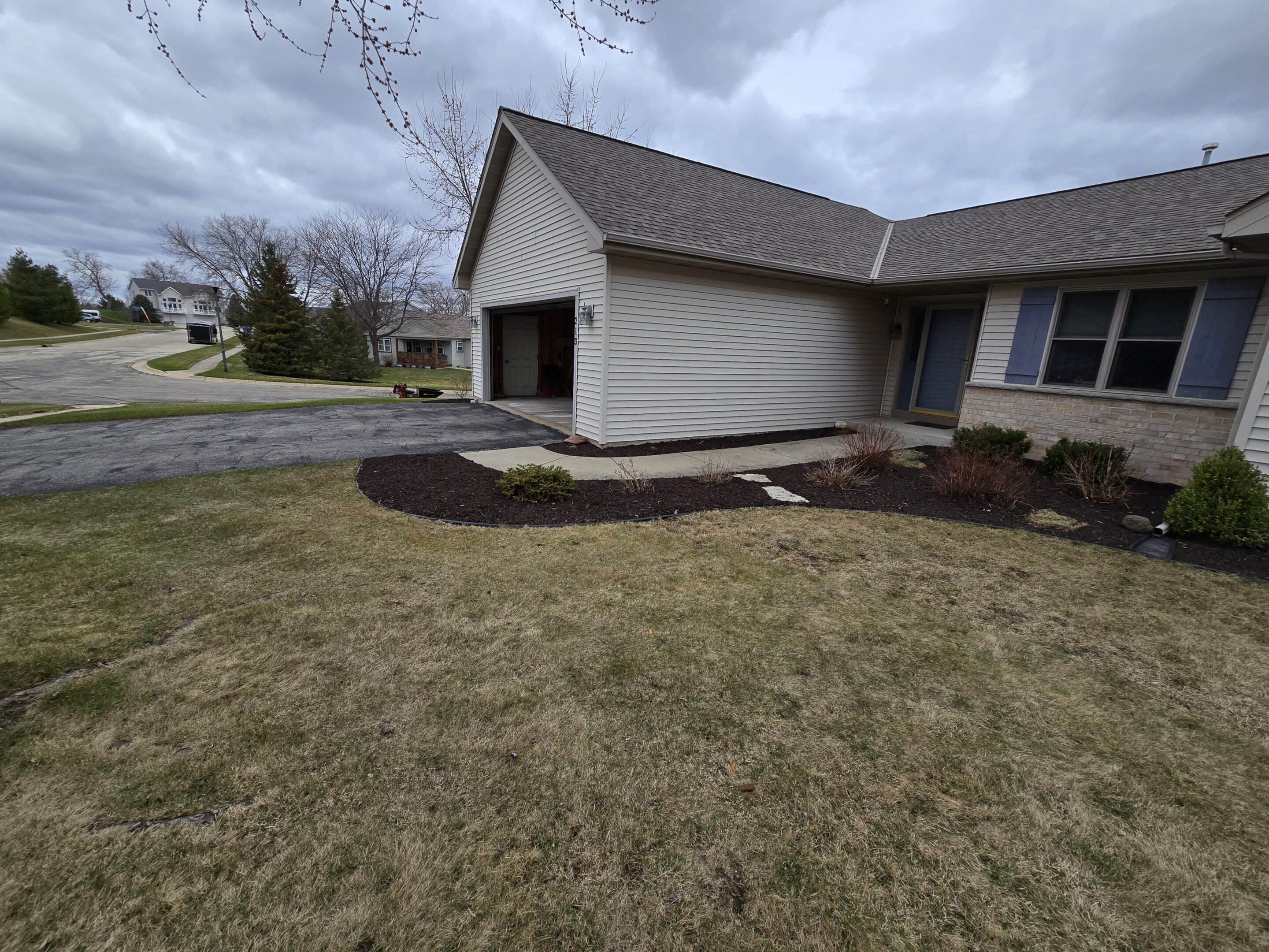 Freshly mulched garden bed next to a suburban house with cloudy sky.
