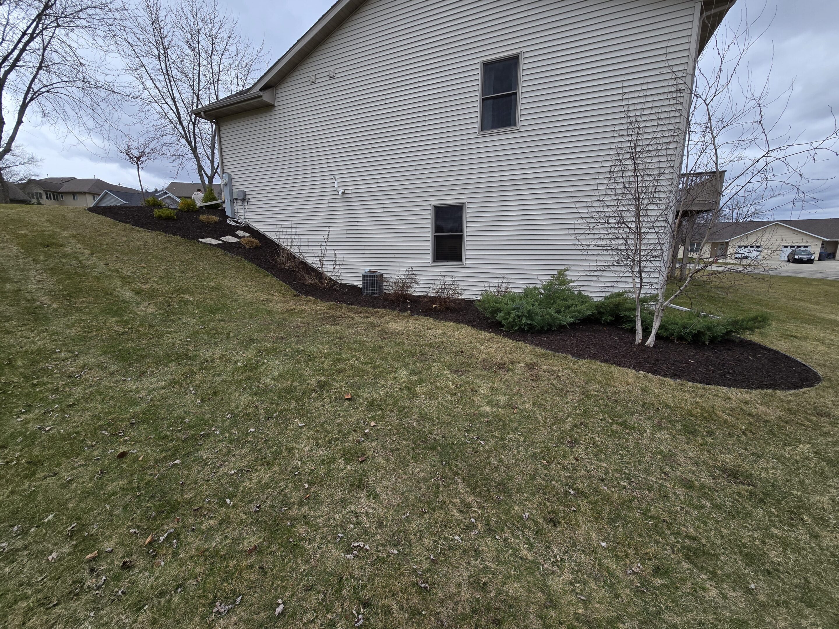 Freshly mulched garden bed along a house's side with a sloped lawn.