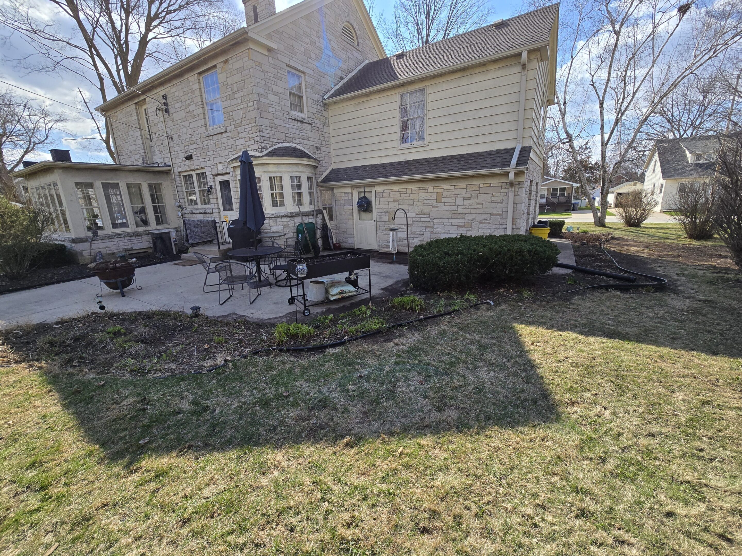 A backyard with stone patio and beige house on a sunny day.