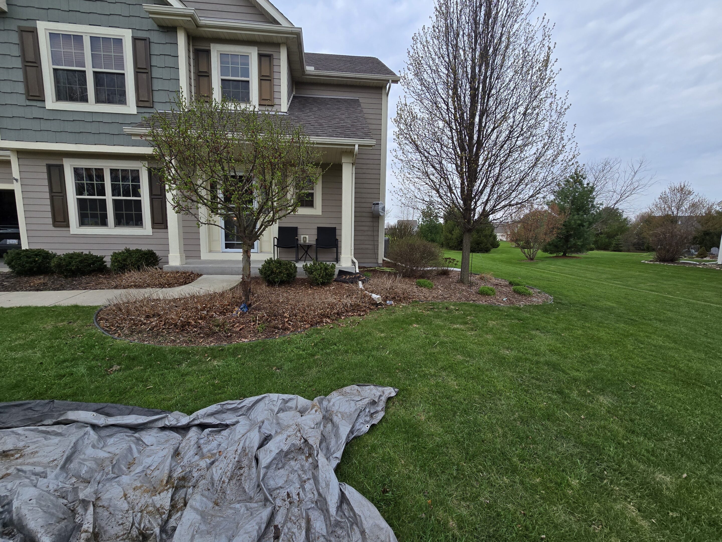 A residential house with a landscaped front yard and a gray tarp on the grass.