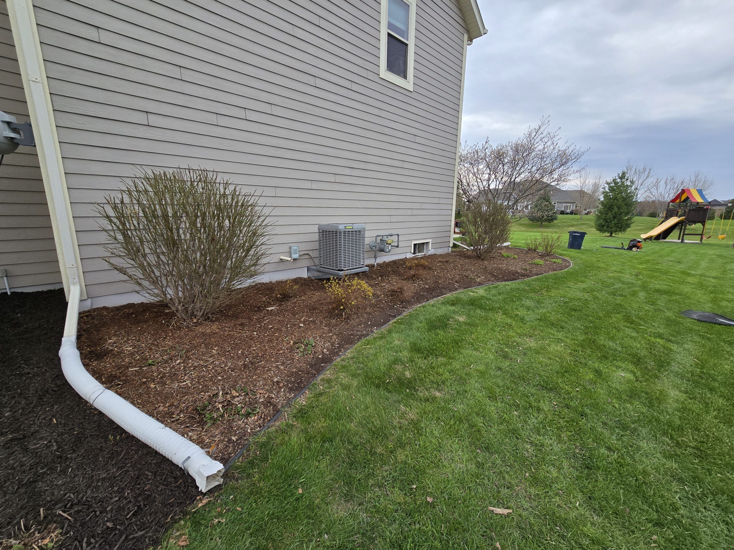 A well-maintained garden bed along a house with mulch and trimmed bushes.