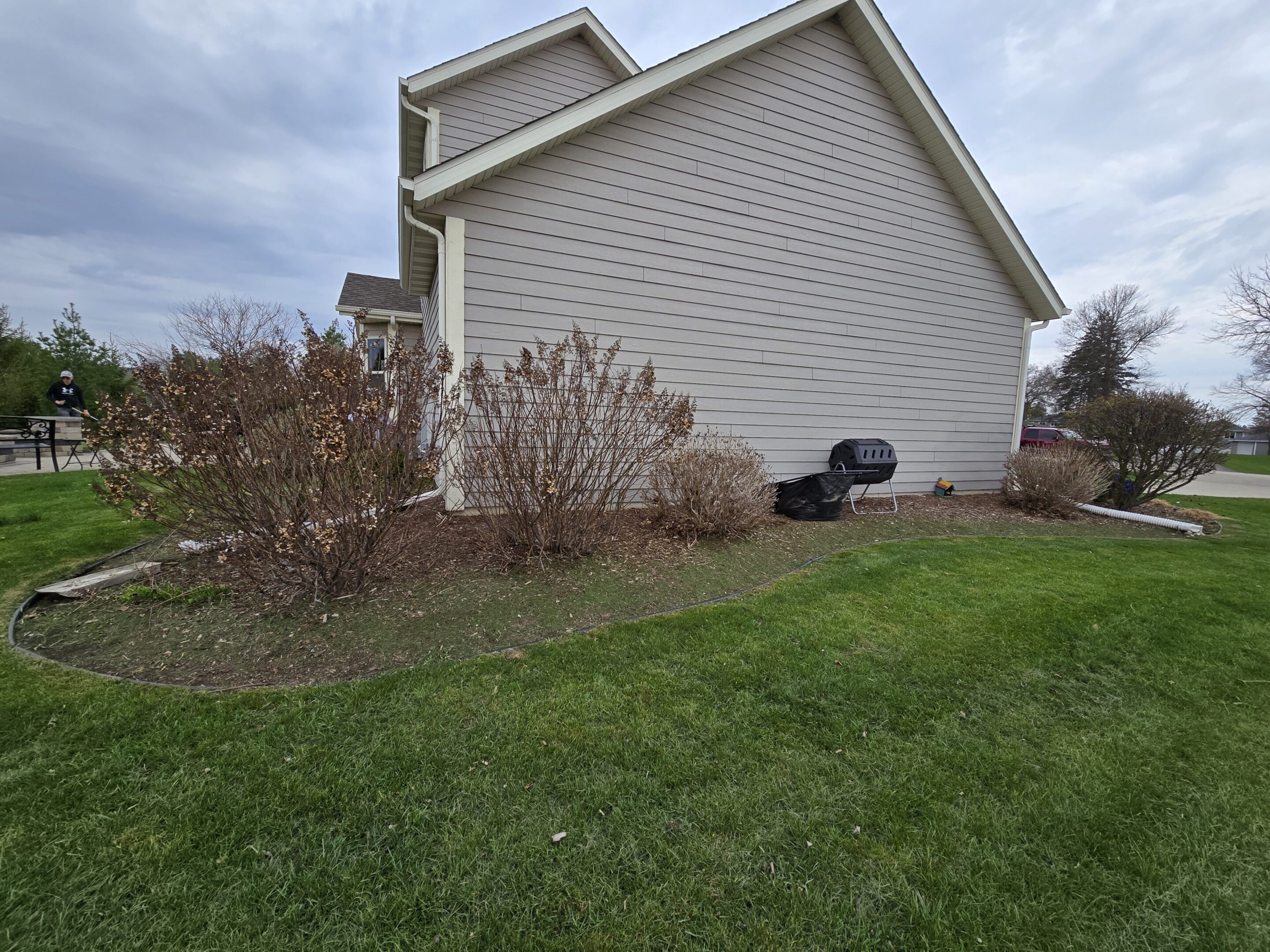 A suburban backyard with green lawn and bushes beside a house.