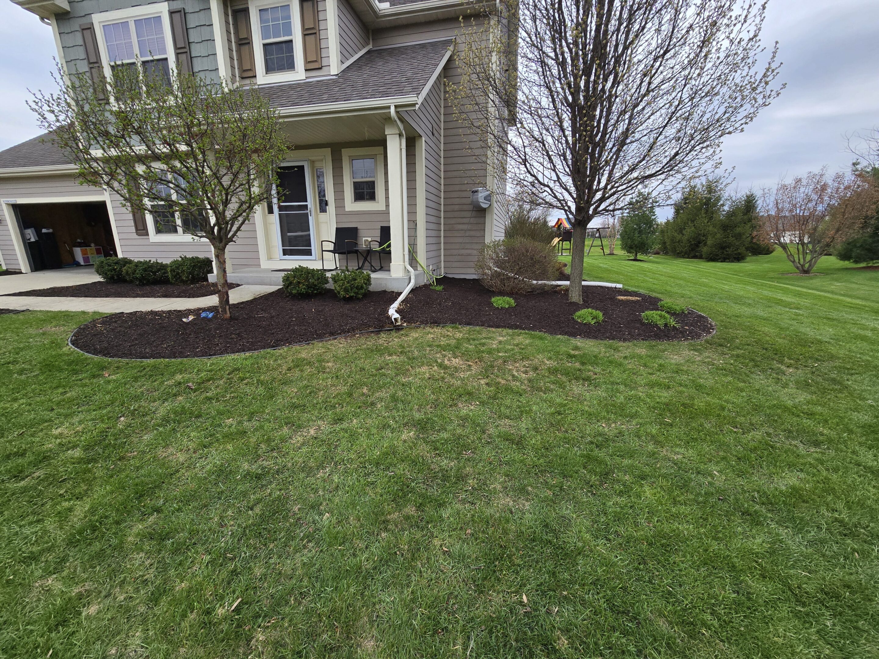 Well-maintained front yard with green grass and fresh mulch beds.