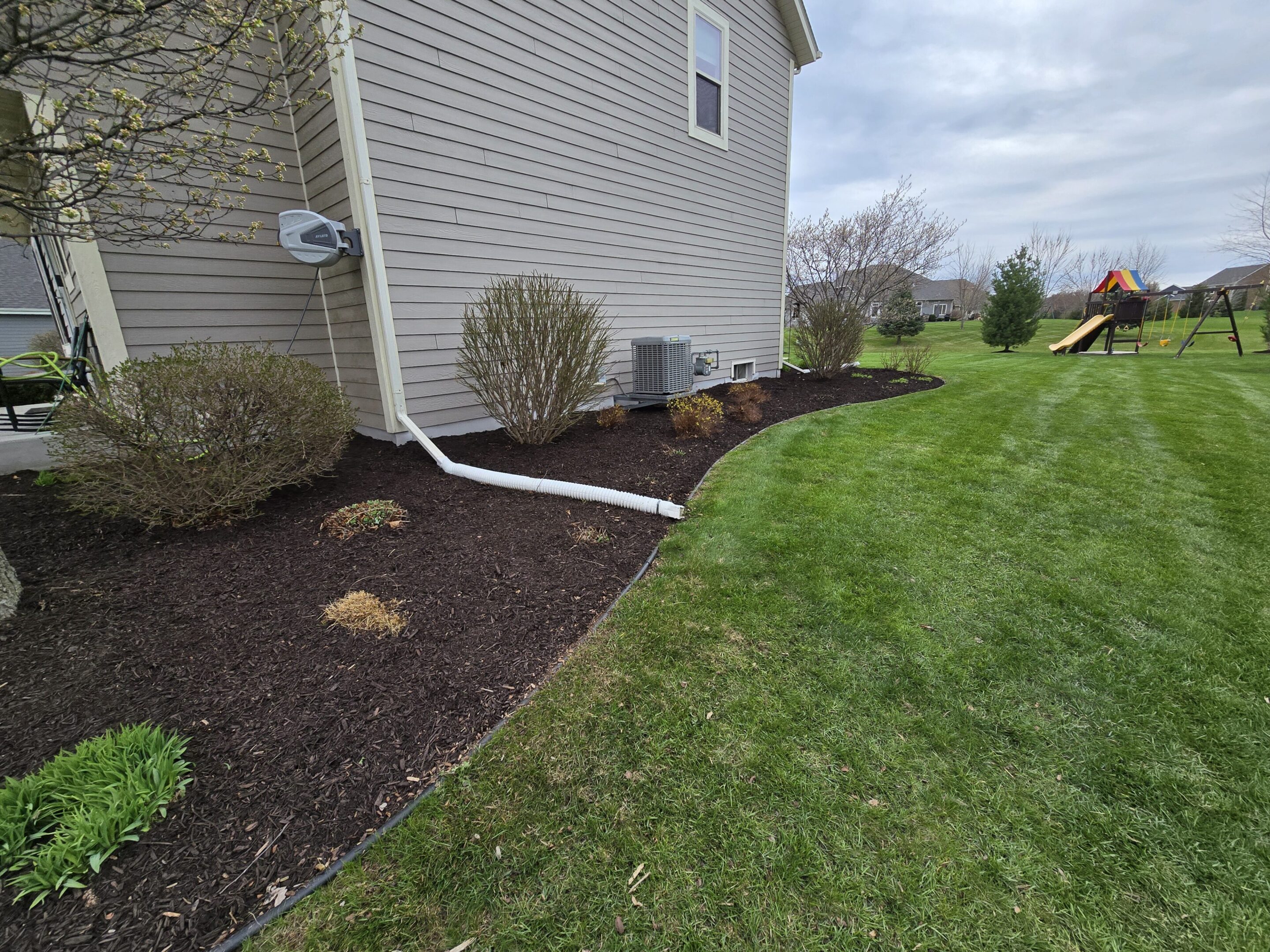 Freshly mulched garden beds alongside a house with neatly trimmed bushes.