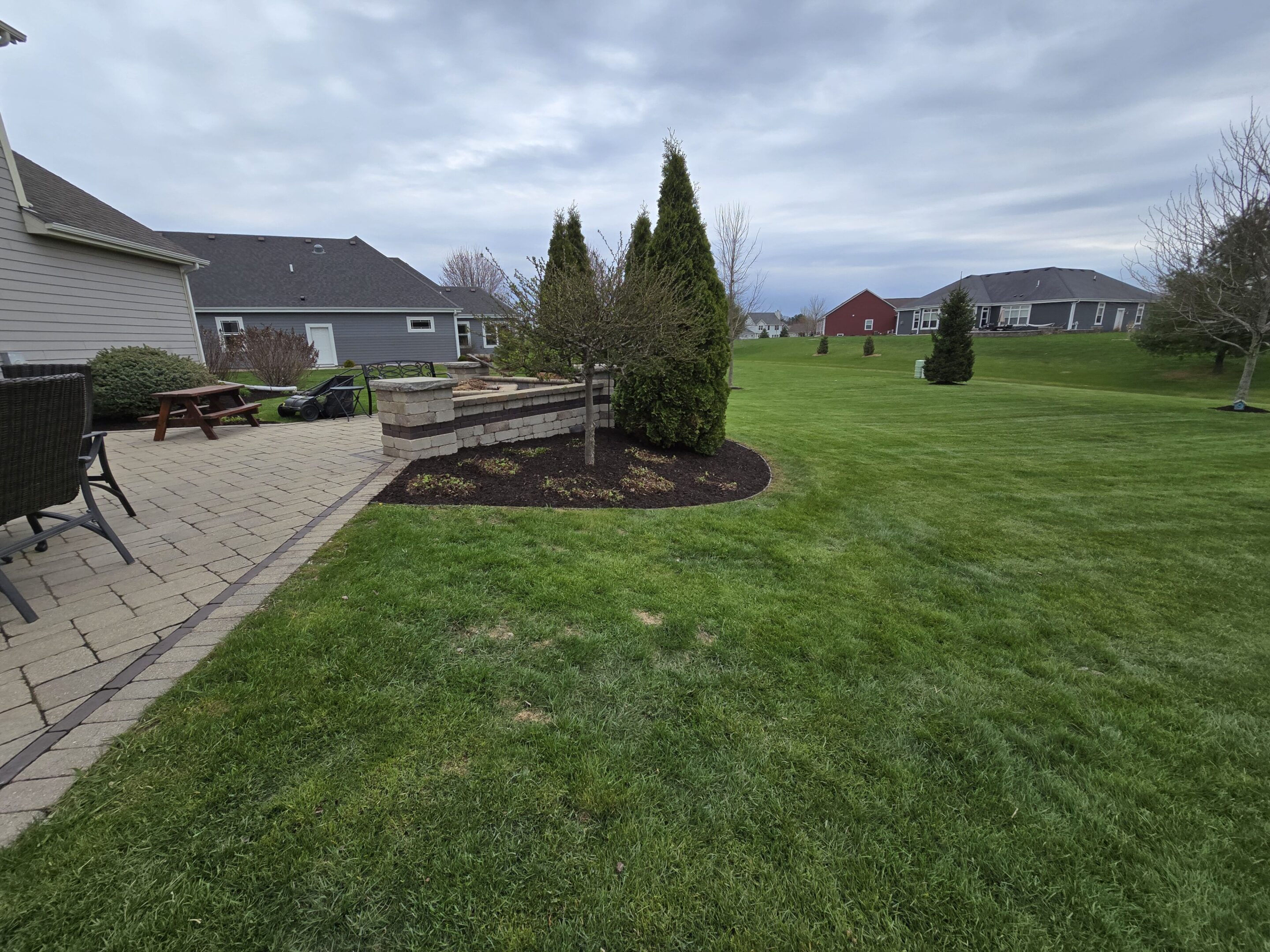 A landscaped garden with grass, shrubs, and a paved pathway beside a house.