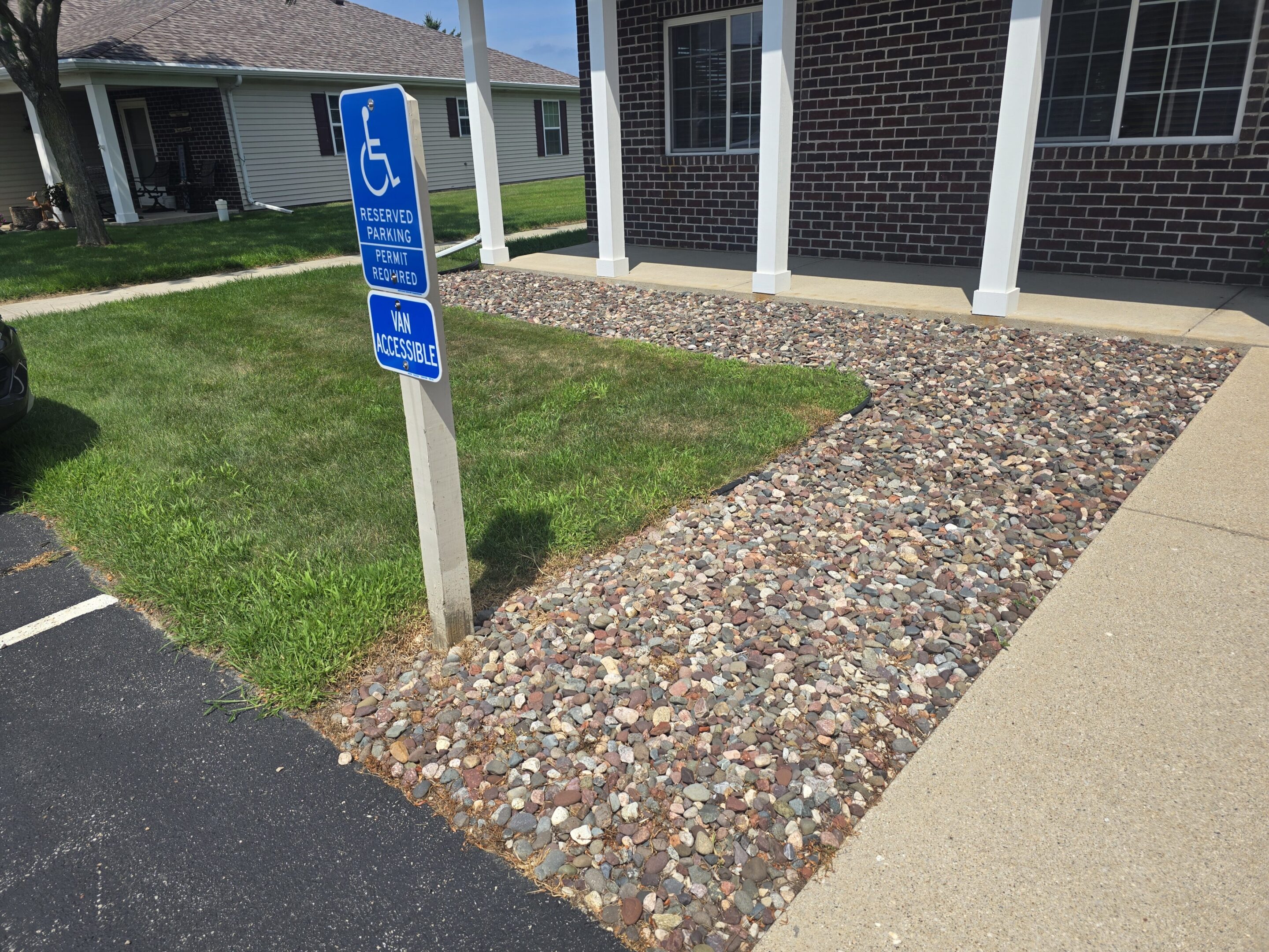 Handicap parking sign next to a stone-filled drainage area by a building.