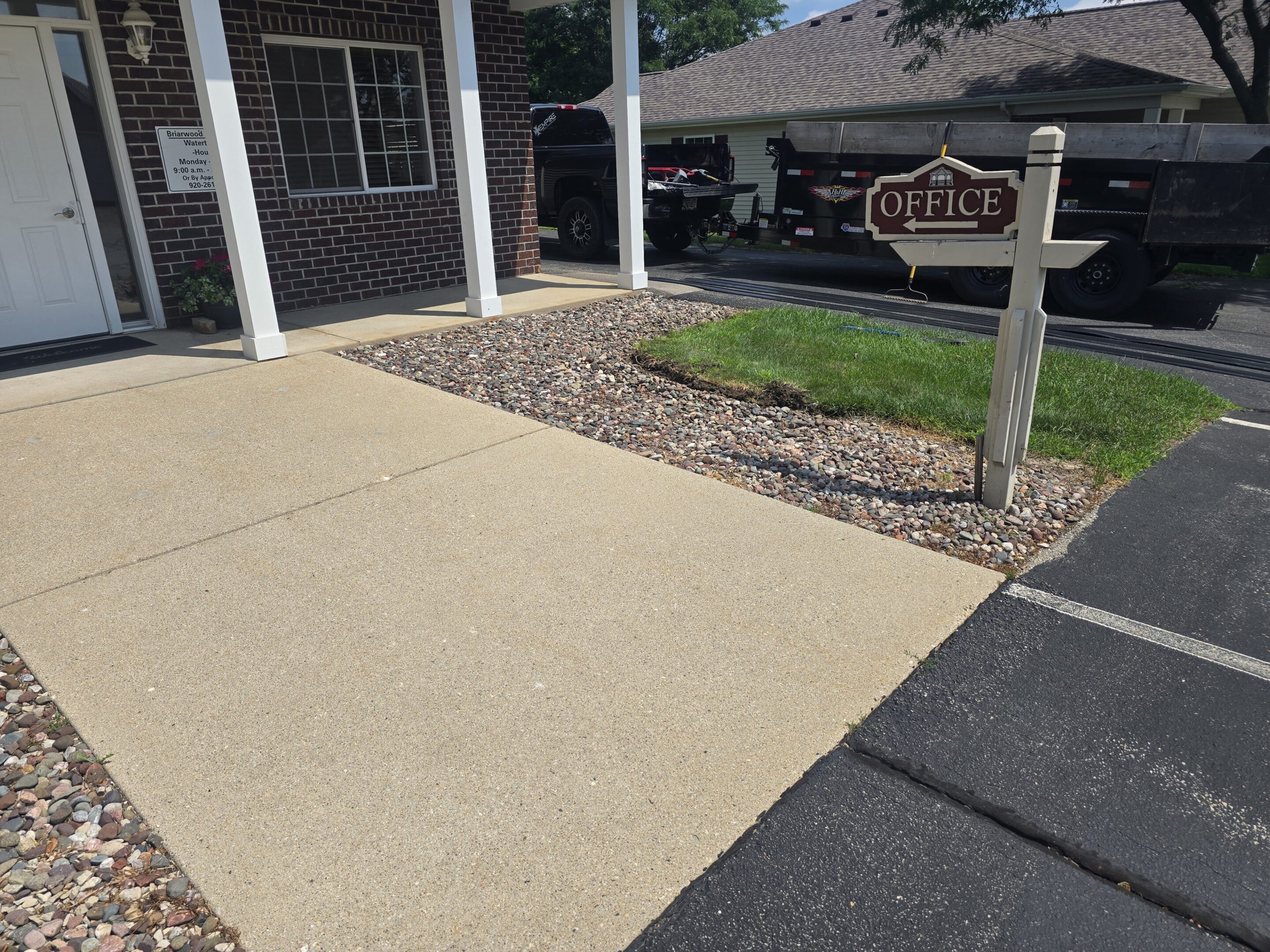 A clean driveway with a gravel strip and a 'For Sale' sign outside a house.