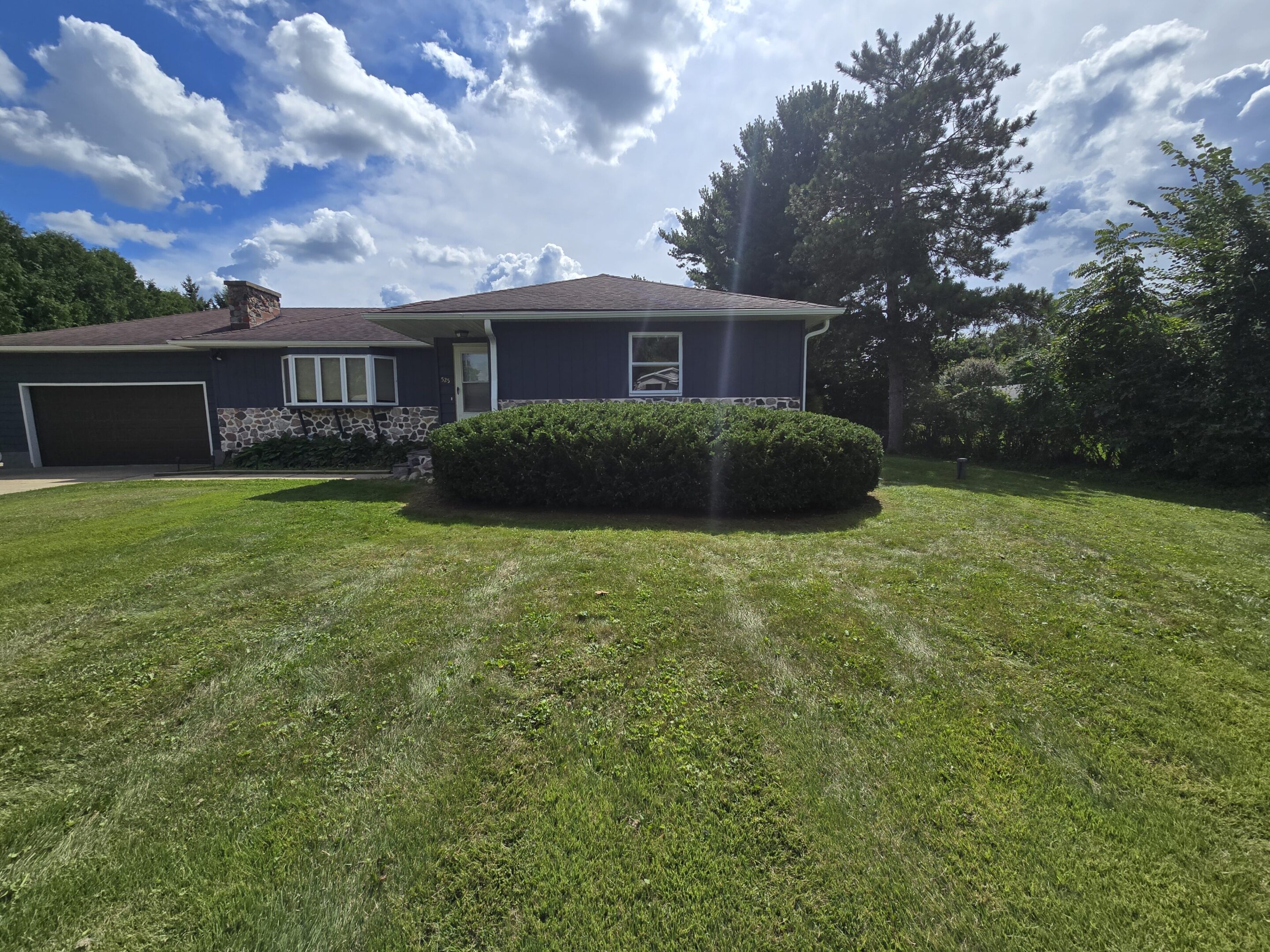 A single-story house with a large green lawn under a partly cloudy sky.