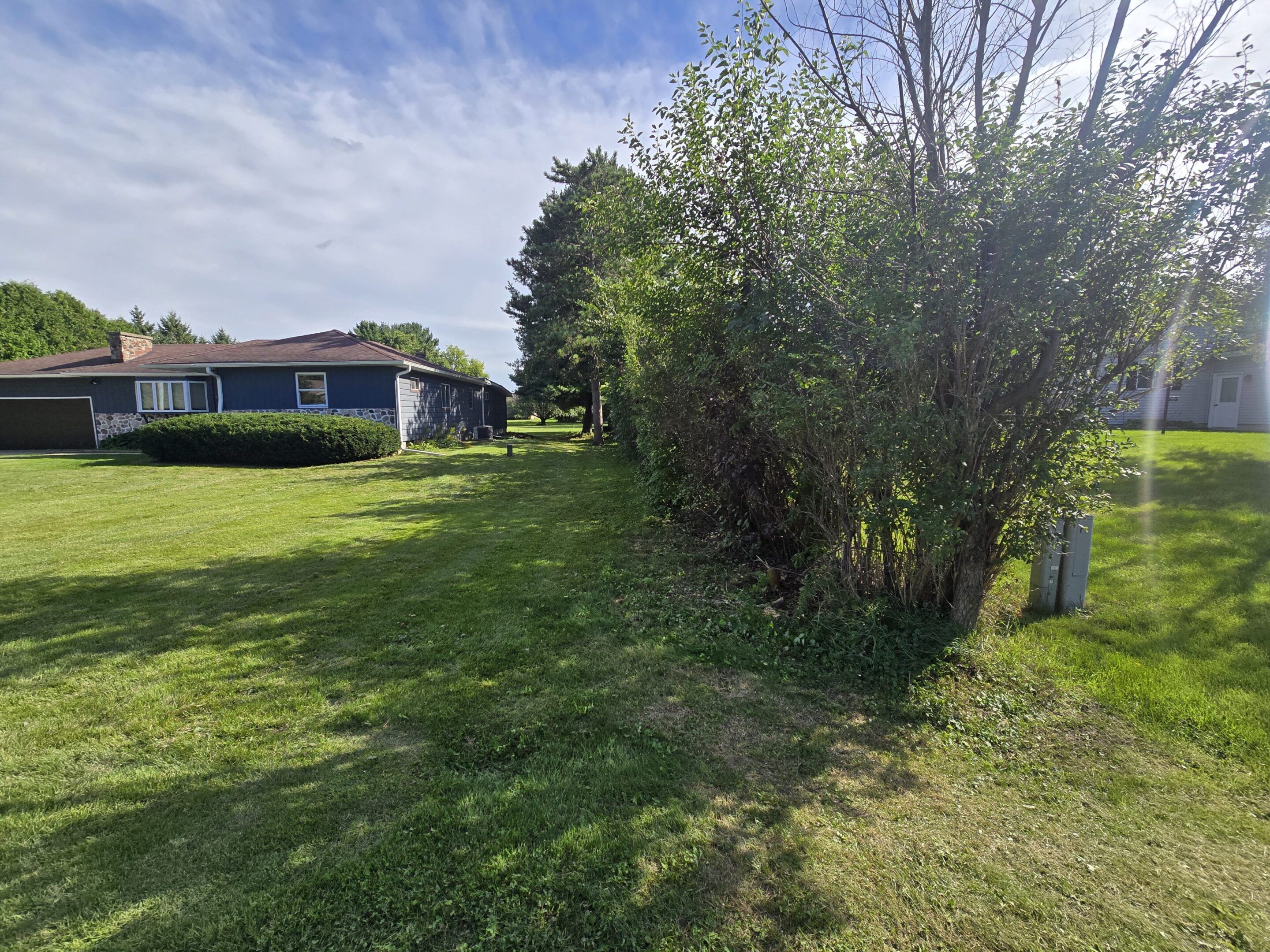 A grassy lawn with trees and a building under a cloudy sky.