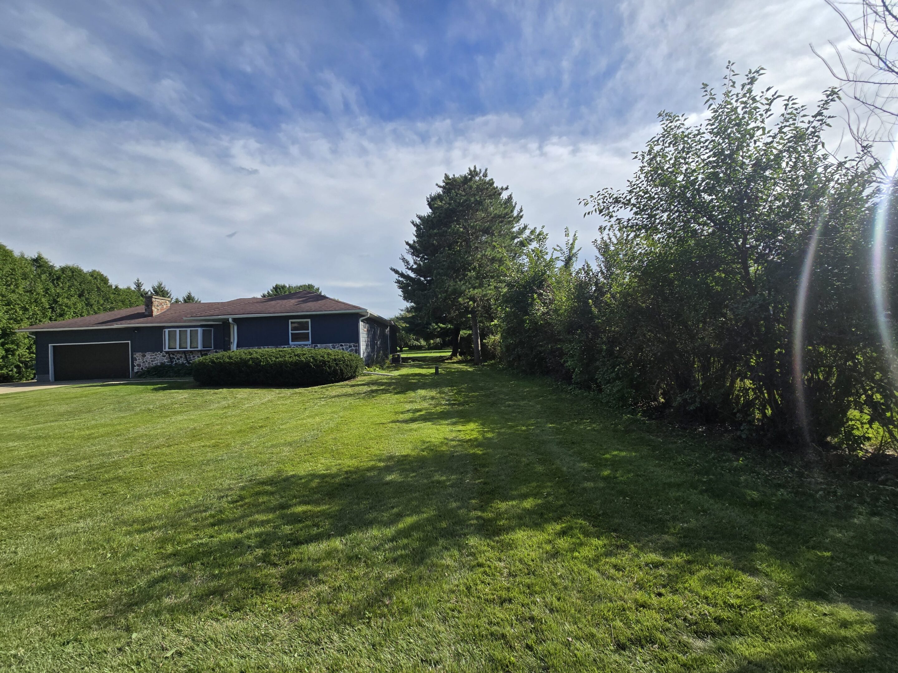 A spacious green lawn with a house and trees under a partly cloudy sky.