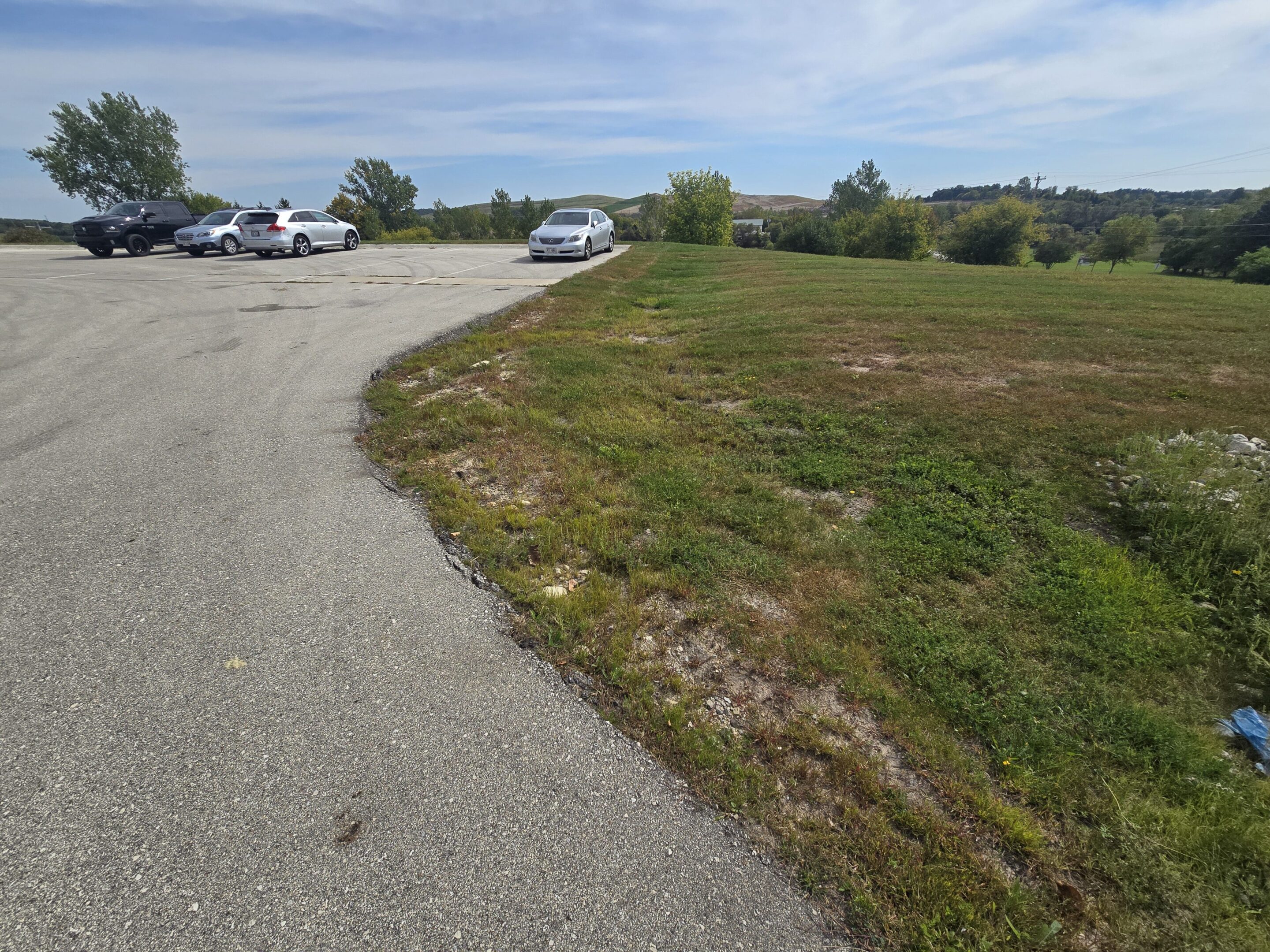 A few cars parked near a grassy area under a cloudy sky.