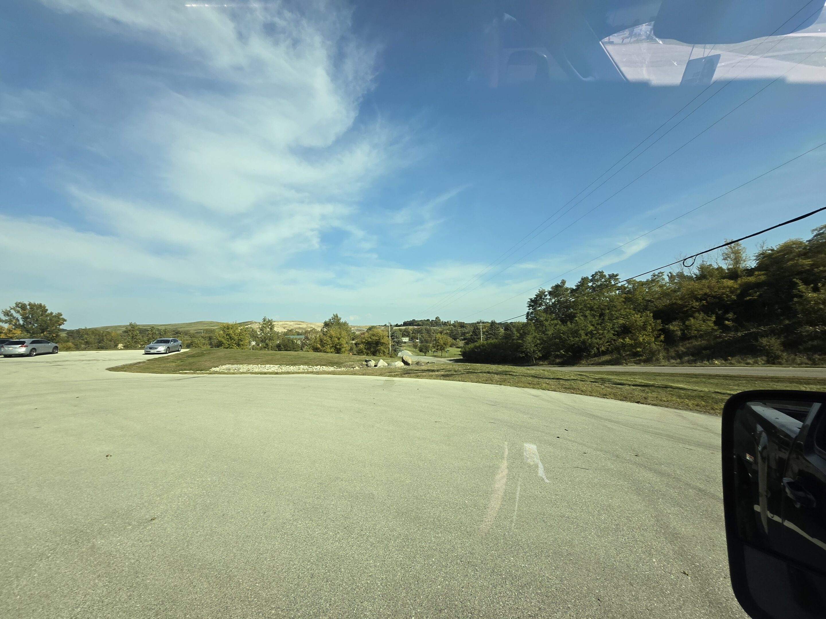 A wide, empty road under a partly cloudy blue sky with trees in the distance.