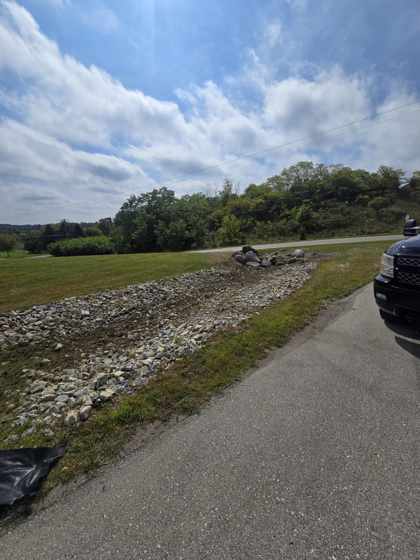 A dirt bike rider on a muddy trail near a road and parked vehicles.