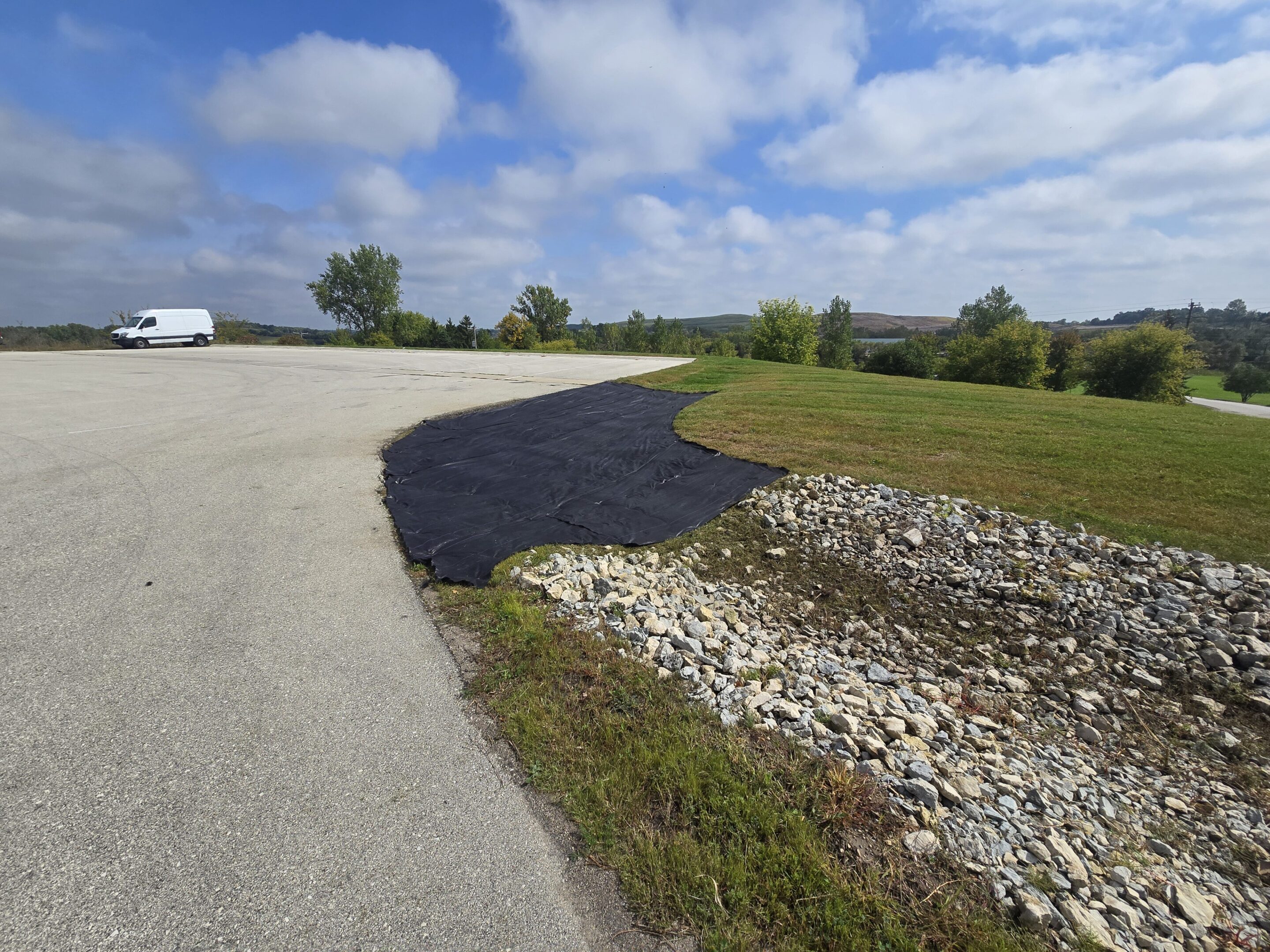 A freshly paved road section next to gravel and grass under a blue sky.