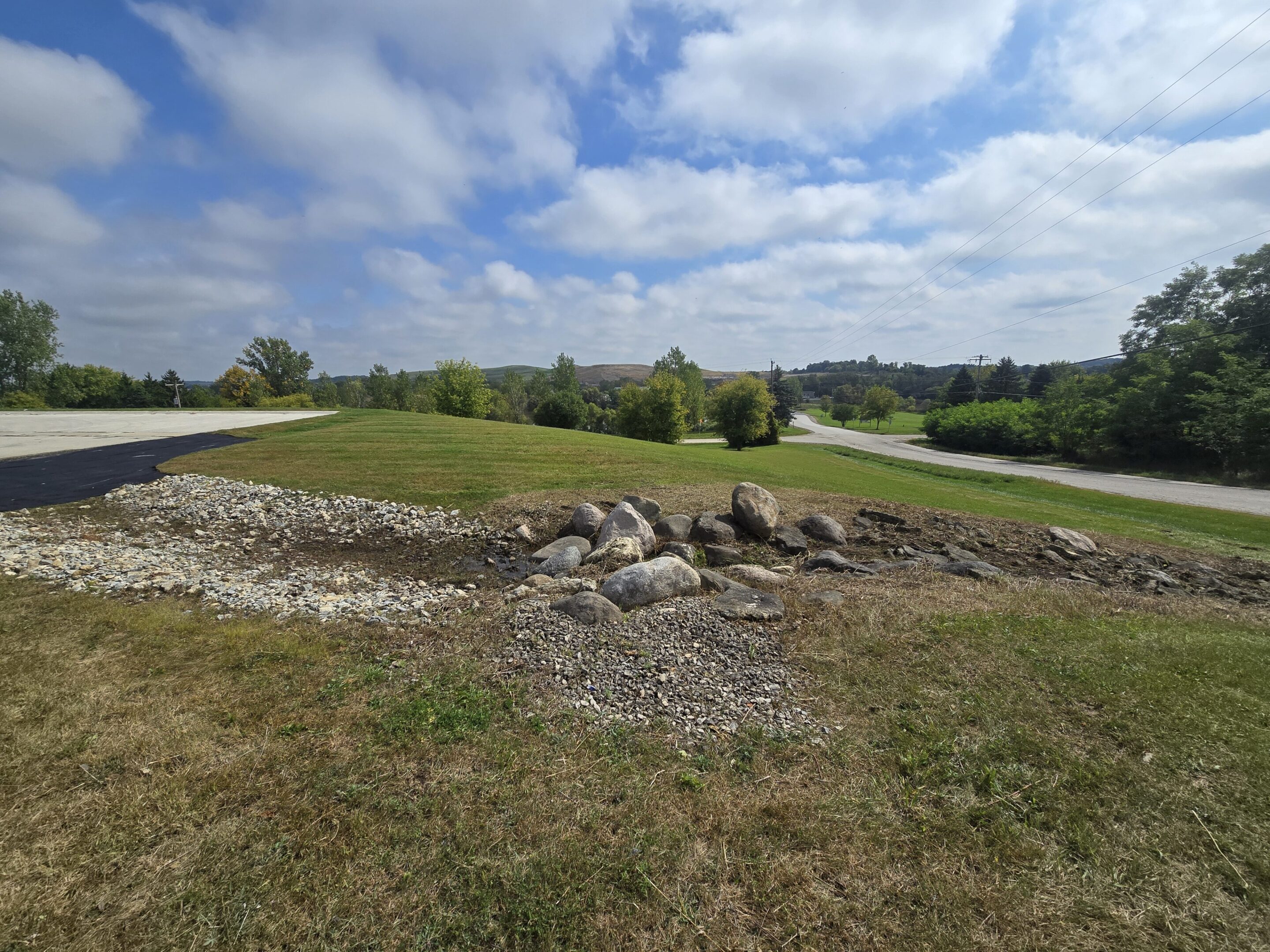 A grassy landscape with a stone border under a partly cloudy sky.