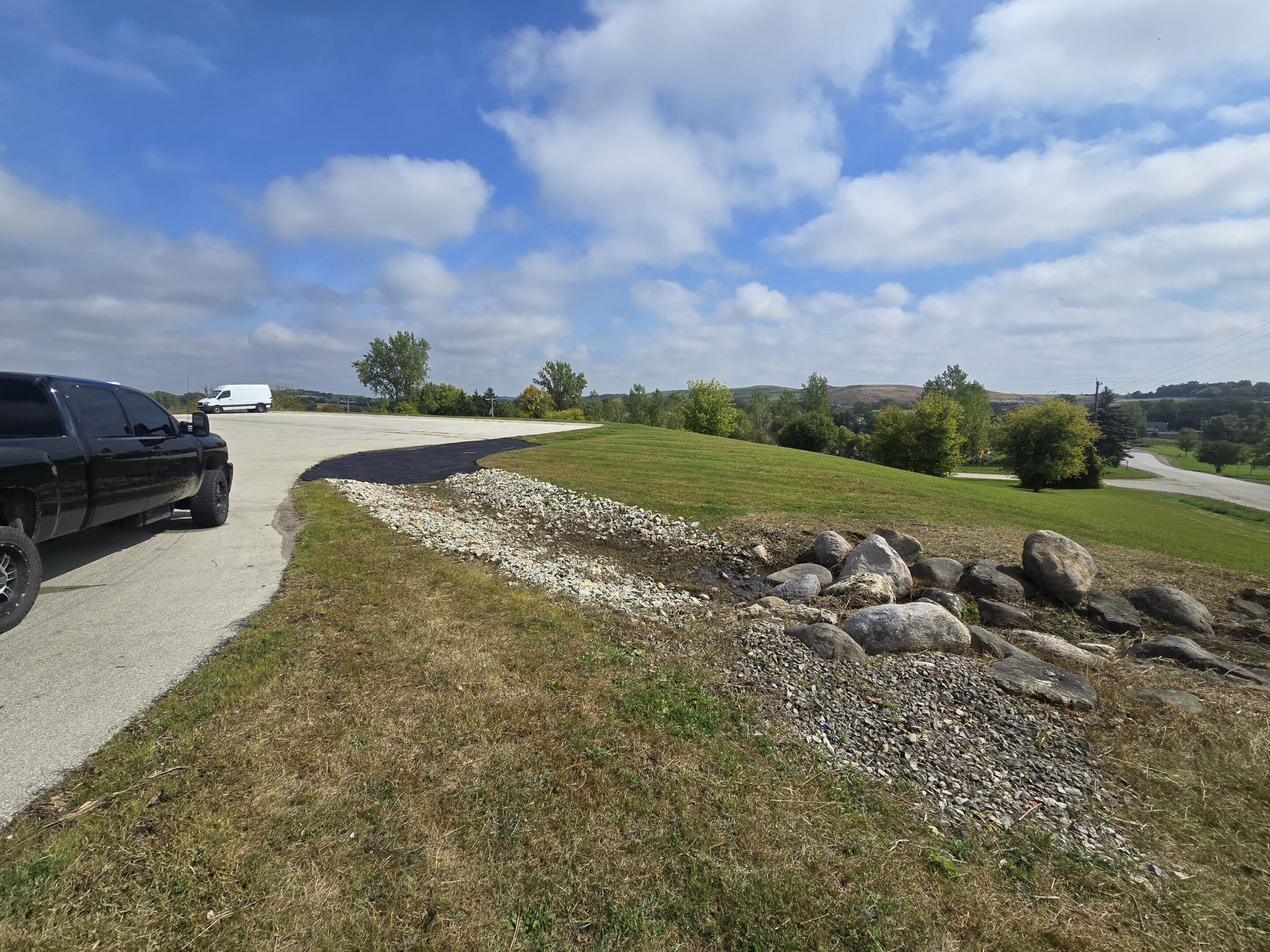 A golf cart parked on a path beside a grassy hill under a blue sky.